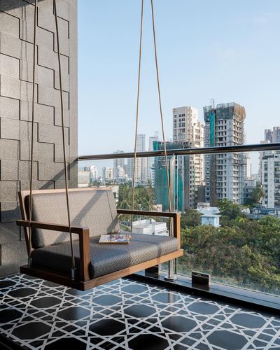 Wooden hanging swing sofa on a balcony overlooking Mumbai skyline with patterned black and white floor tiles