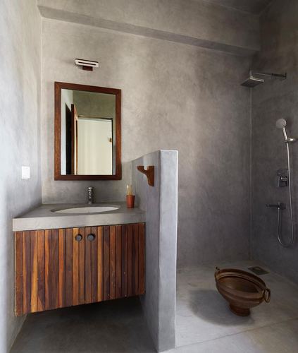 Concrete bathroom with wooden slatted vanity, mirror, and open shower behind a low partition wall