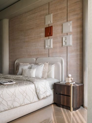 Bedroom corner with curved upholstered headboard, dark wood nightstand, and textured wall panels with sculptural reliefs