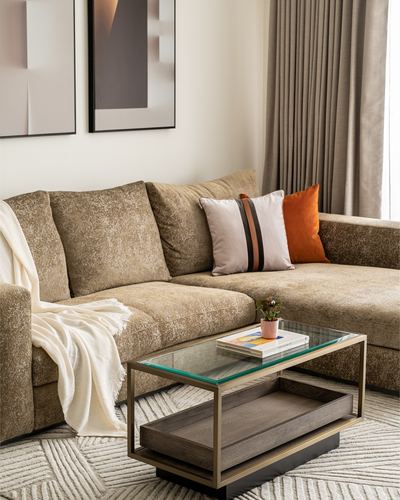Beige textured sectional sofa with orange and neutral cushions beside a glass and wood coffee table