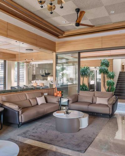 Living room with two taupe leather sofas, round marble coffee table, checkered ceiling and glass wall to courtyard.