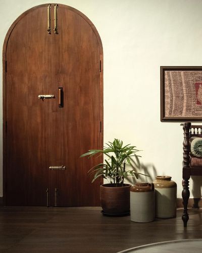 Arched wooden door with brass bolts beside potted palm and ceramic jars against cream wall