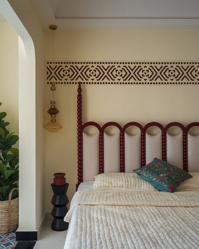 Bedroom with maroon scalloped headboard, patterned wall border, and hanging brass pendant lights
