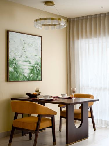 Dining nook with mustard velvet chairs, dark wood table, green abstract painting, and ring chandelier