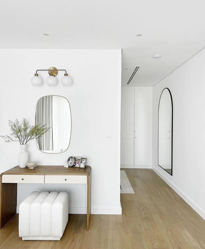 White entry hallway with wood vanity table, oval mirror, and arched floor mirror down corridor