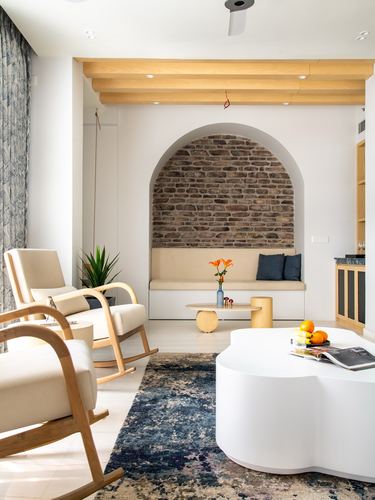 Living room with arched exposed brick niche, cream rocking chairs, and curved white coffee table on navy rug