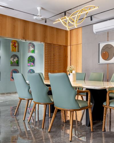 Dining room with marble table, sage green chairs, wood panelling, and a gold sculptural pendant light