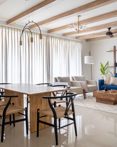 Open dining and living space with wood beam ceiling, wishbone chairs, and sheer curtains