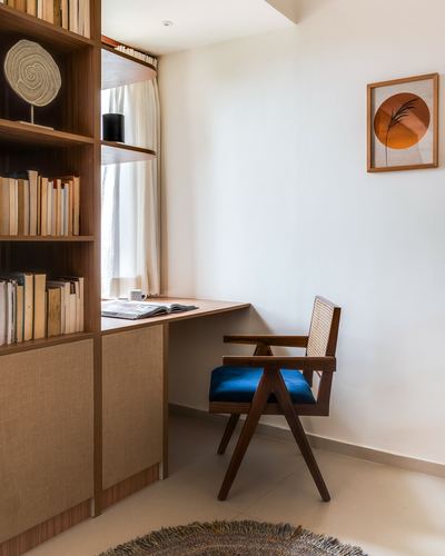Study nook with cane-back chair, blue seat cushion, built-in wood desk and bookshelf, framed circular art