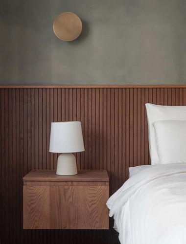 Bedroom corner with sage plaster wall, fluted wood paneling, floating nightstand, and white bedding