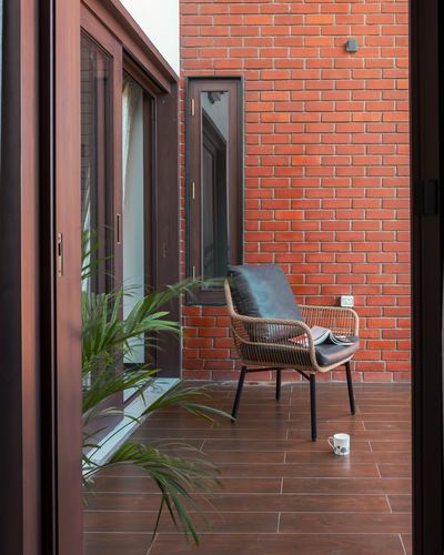 Brick-walled balcony corner with rattan chair, mug, plants, seen through open wooden sliding doors