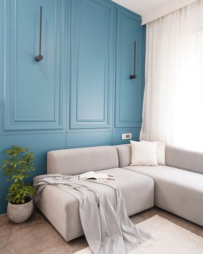 Grey sectional sofa against a teal paneled wall with sheer curtains