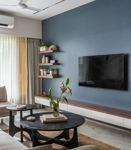 Living room with blue accent wall, wall-mounted tv, floating wood shelves and sculptural black coffee tables