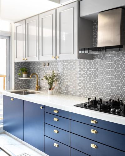 Modern kitchen with navy lower cabinets, white upper cabinets, geometric tile backsplash and gas hob