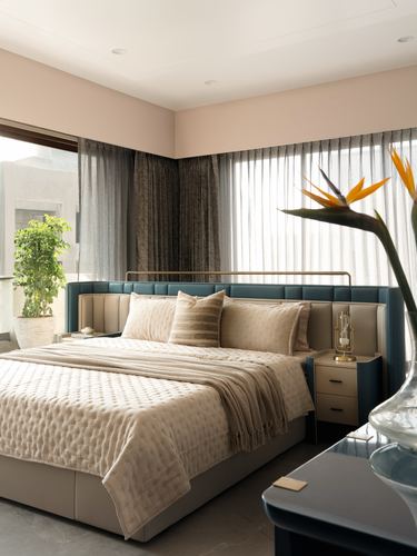 Modern bedroom with teal leather headboard, cream bedding, sheer curtains and bird of paradise flower