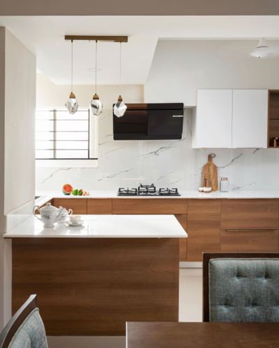 Modern kitchen with wood cabinetry, marble-look backsplash, black chimney hood and cluster pendant lights