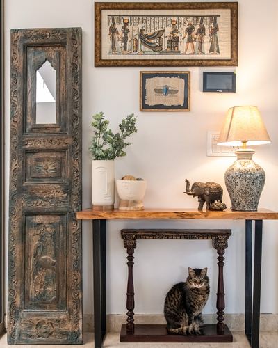 Foyer vignette with carved wooden door panel, Egyptian art, and a live-edge console table with a cat beneath