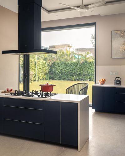Navy kitchen island with hob and hood facing a large window overlooking a green garden