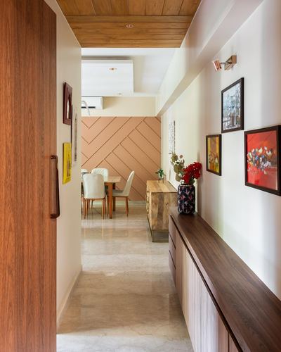 Hallway with wood ceiling, marble floor, framed art wall, leading to dining area with herringbone panel