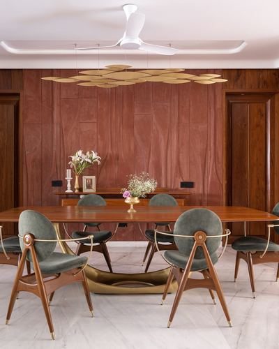 Dining room with wood-panelled wall, brass chandelier, and green velvet chairs around a wooden table