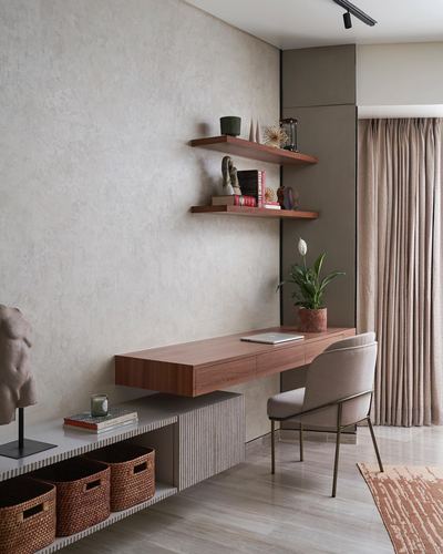 Floating wood desk and shelves against textured plaster wall with curtain and rattan baskets below