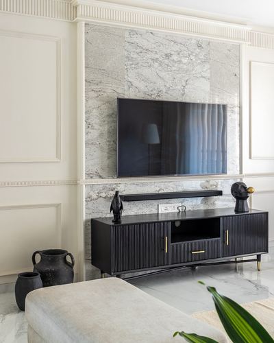 Living room with marble-clad wall, wall-mounted tv, and fluted black tv console with brass handles