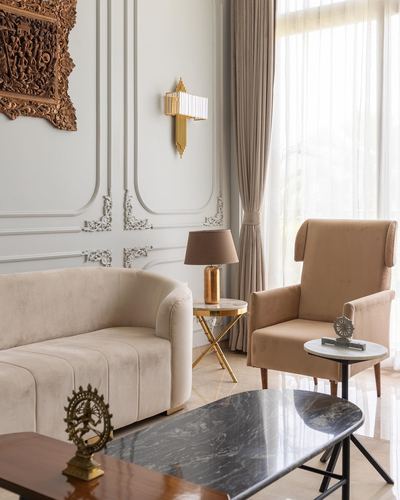 Beige living room with panelled walls, art deco sconce, velvet sofa and armchair, marble tables