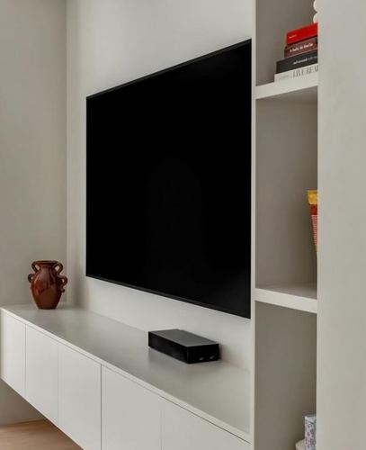 Minimalist bedroom wall with mounted tv, floating white cabinet, and built-in shelving with vase and books