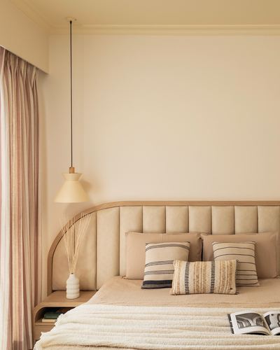 Beige bedroom corner with arched tufted headboard, pendant lamp, and striped curtain