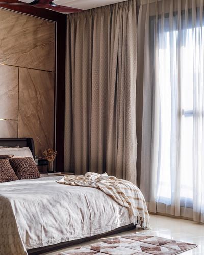 Bedroom with marble-look headboard wall, layered curtains, and soft window light on white bedding