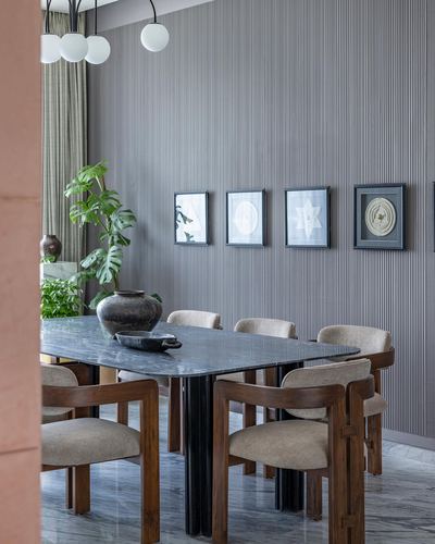 Dining room with dark stone table, curved wood chairs, and framed art gallery wall