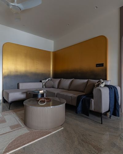 L-shaped grey sofa in living room with gold ombre corner wall and round ribbed coffee table