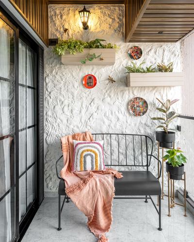 Balcony nook with black bench, peach throw, and textured white wall styled with planters and art plates