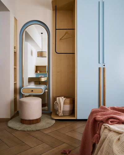 Powder blue wardrobe beside arched mirror vanity with pouf on herringbone wood floor