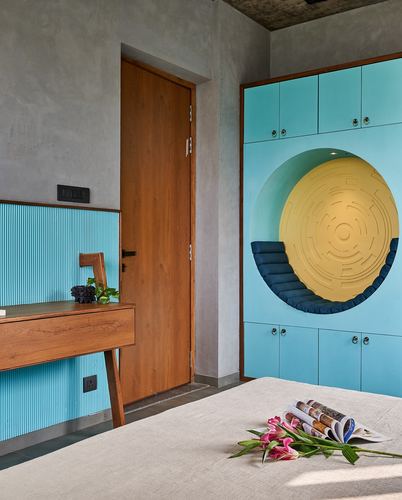 Blue wardrobe wall with circular mustard niche and cushioned seat beside a wooden door and desk