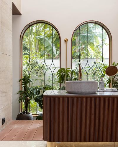 Bathroom with fluted wood vanity, stone vessel sink, and arched windows overlooking greenery
