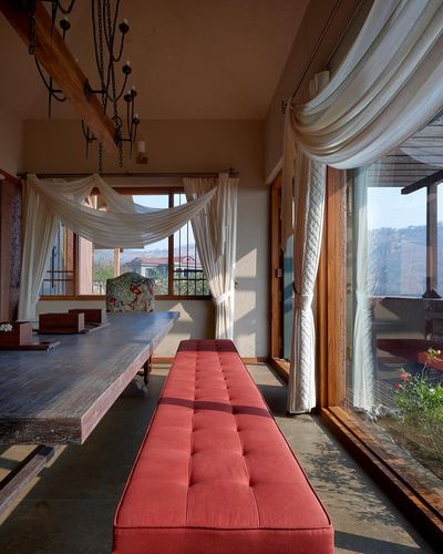 Rustic dining room with red tufted bench, wooden table, and sheer curtains framing valley view