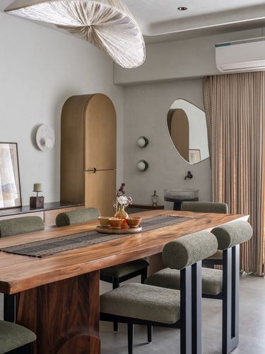 Dining room with live-edge wood table, sculptural pendant, arched brass cabinet, and round mirror