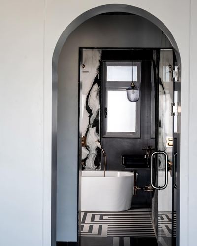 View through arched doorway into black marble bathroom with white tub and pendant light