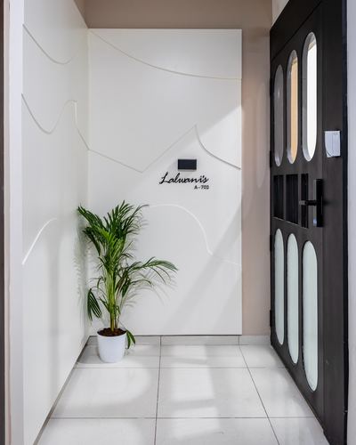 Minimalist white entry foyer with sculpted wave wall, plant, and dark oval-glass door