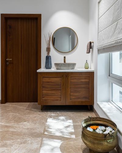 Bathroom vanity with round mirror, stone vessel sink, louvered wood cabinet, and marble floor