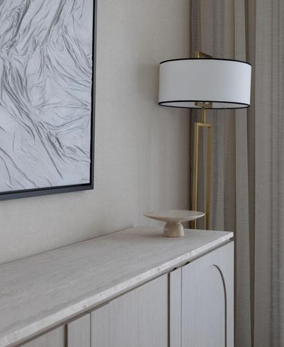 Corner vignette of a sideboard with travertine top, oak cabinetry, brass floor lamp and textured artwork