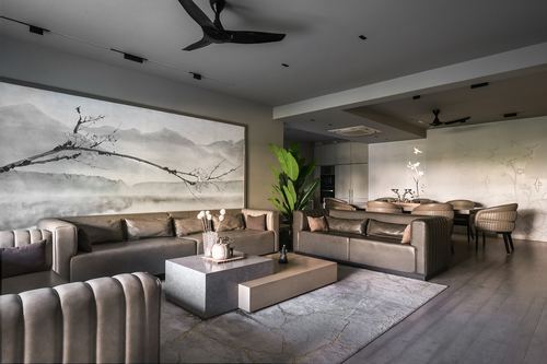 Grey channel-tufted sofas around stone coffee tables beneath a large ink landscape mural, dining area beyond