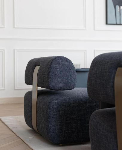 Close-up of a dark navy upholstered armchair with a brass metal side frame against a white paneled wall