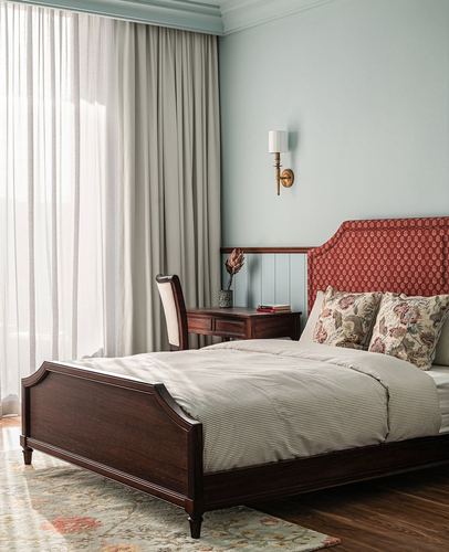 Bedroom with dark wood bed, red patterned headboard, sheer curtains, and brass sconce