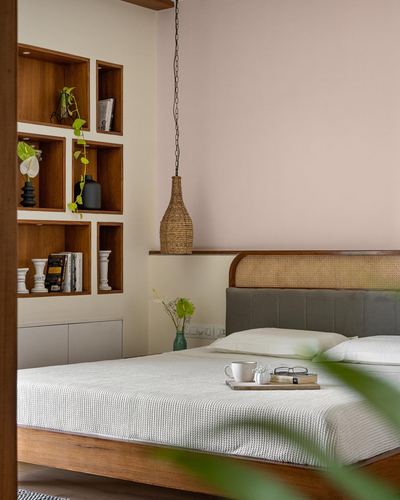 Bedroom with cane headboard bed, woven pendant light, and wooden cubby shelves displaying vases and books