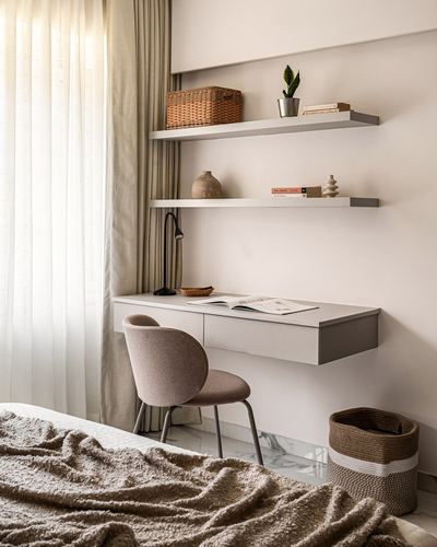 Wall-mounted desk under floating shelves with a pink upholstered chair beside a curtained window