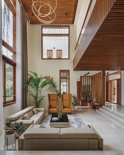 Double-height living room with wood slat ceiling, mustard armchairs, and beige sectional on marble floor
