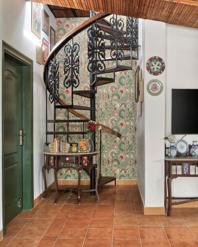 Wrought-iron spiral staircase in a terracotta-tiled foyer with floral wallpaper and a green door