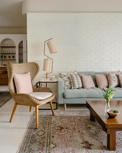 Living room with cane wingback chair, sage sofa, brass floor lamp, and wooden coffee table on patterned rug